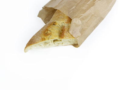 Freshly baked French baguette in a paper bag. Traditional homemade white bread wrapped in rustic brown paper. Isolated on a white background. Close-up. With clipping path. Copy spaceの写真素材