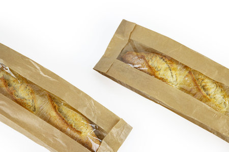 Two freshly baked baguettes, wrapped in brown paper bag, Artisan French baguettes with crispy crusts in paper packaging. Isolated on a white background. Close-up. Copy spaceの写真素材
