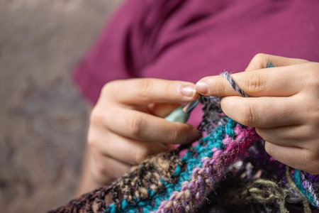 Young woman's hands crochet colorful yarn with crocheting hook. Closeup details of handmade needlework art project and creative crafting techniques. Handmade textile artist knitting with yarn.の写真素材