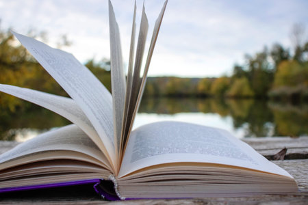 Open book with pages flipping in the wind. Reading on the lake wooden dock on autumn day. Learning...
