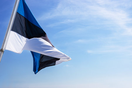 National Estonian flag waving against a partly cloudy sky, symbolizing national pride and identity with distinct horizontal blue, black, and white stripes. Copyspaceの写真素材