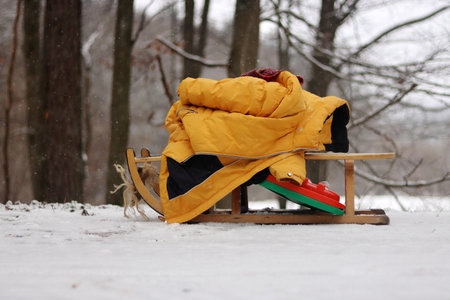 Clolseup of a wooden sled with a warm yellow jacket on a snowy ground in the woods, depicting a winter scene and peaceful retreat into a snow-covered forest. Copy spaceの写真素材