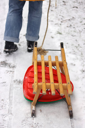 Young woman in yellow jacket pulling a wooden sled on a snowy path by a road. Teenage girl on a winter walk in forest with snow covered trees, outdoor stroll on a quiet snowy day.の写真素材