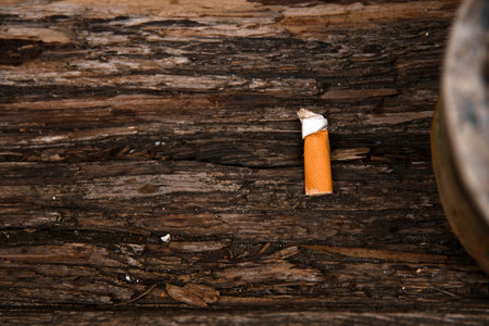 Closeup of an ashtray filled with numerous cigarette butts on a wooden surface, symbolizing smoking habits and litter, smoking harm, urban pollution, unhealthy lifestyle, littering.の写真素材