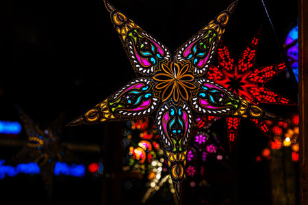 Handcrafted Christmas star lantern with intricate ornament, lighting up a bustling Christmas market with vibrant colors, creating a cozy holiday atmosphereの写真素材