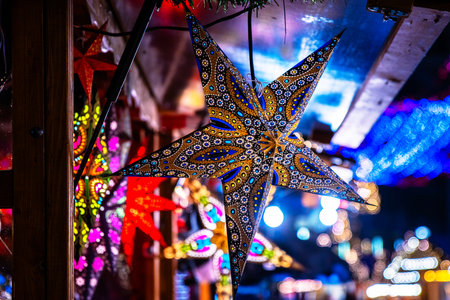 Handcrafted star lanterns hanging at beautifully lit Christmas market. Colorful lights and wooden stalls creating a magical holiday atmosphere at nightの写真素材