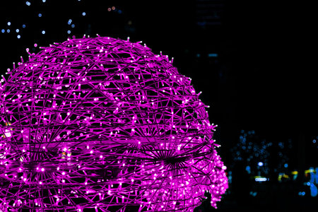 Closeup of intertwined pink magenta purple lilac neon string lights next to Christmas market. Crisscrossing glowing LED garland with small bright bulbs against dark background. Copy spaceの写真素材