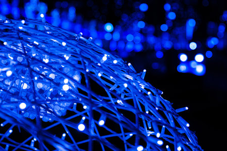 Closeup of intertwined blue neon string lights on the street next to Christmas market. Crisscrossing glowing LED garland with small bright bulbs against dark background. Copy spaceの写真素材