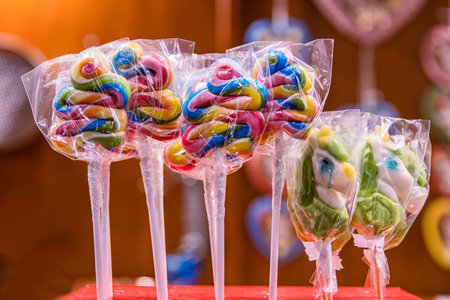 Colorful lollipops in swirled shapes wrapped in plastic, displayed on a sweet treats stand. Multicolored candies offered at seasonal marketの写真素材