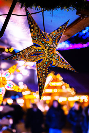 Handcrafted star lanterns hanging at beautifully lit Christmas market. Colorful lights and unrecognizable people on blurred background.の写真素材