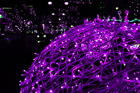 Closeup of intertwined pink magenta purple lilac neon string lights next to Christmas market. Crisscrossing glowing LED garland with small bright bulbs against dark background. Copy spaceの写真素材