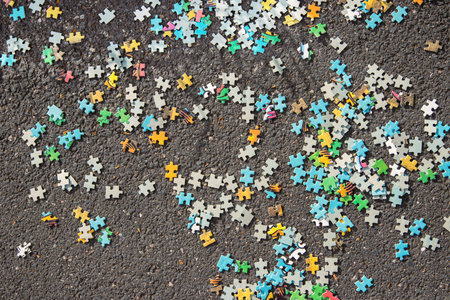 Colorful jigsaw. Unfinished scattered puzzle pieces spread on the gray asphalt pavement on the street. Messy chaotic concept. Close up. Selective focus. Blurred.の写真素材