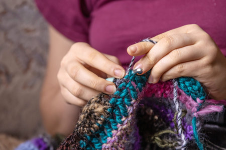 Young woman's hands crochet colorful yarn with crocheting hook. Closeup details of handmade...