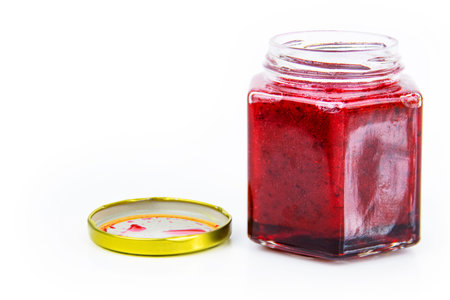 An open hexagonal glass jar of homemade red currant berry or cranberry jam with a gold lid next to...