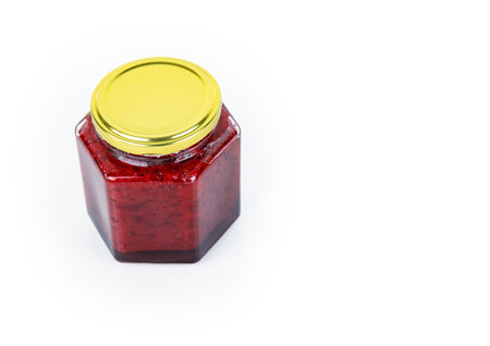 A hexagonal glass jar of homemade red currant berry or cranberry jam sealed with a gold colored metal lid. Freshly made wild berries jelly. Copy space. Isolated on white background.の写真素材