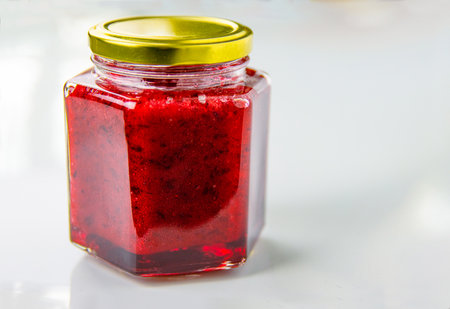 A hexagonal glass jar of homemade red currant berry or cranberry jam sealed with a gold colored metal lid. Freshly made wild berries jelly. Copyspace.の写真素材