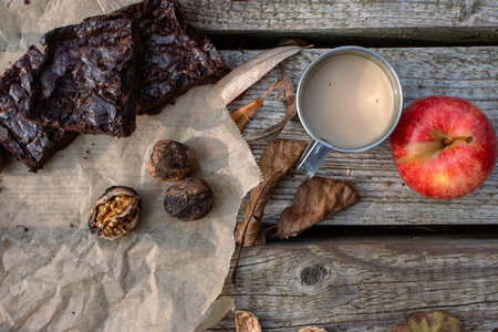 Rustic outdoor snack with fresh apples, brownies, and nuts on a wooden table and a warm coffee in a metal mug. Nature lovers autumn picnic. Top view. Flat lay.の写真素材