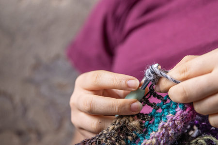 Young woman's hands crochet colorful yarn with crocheting hook. Closeup details of handmade needlework art project and creative crafting techniques. Handmade textile artist knitting with yarn.の写真素材