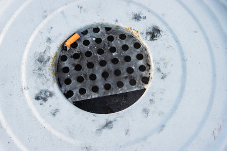 Closeup of a discarded cigarette butt stuck in a rusted metal grate of garbage bin. Nonsmoking, smoking harm, urban pollution, healthy and unhealthy lifestyle, littering, environmental concept.の写真素材
