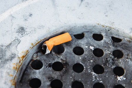 Closeup of a discarded cigarette butt stuck in a rusted metal grate of garbage bin. Nonsmoking, smoking harm, urban pollution, healthy and unhealthy lifestyle, littering, environmental concept.の写真素材