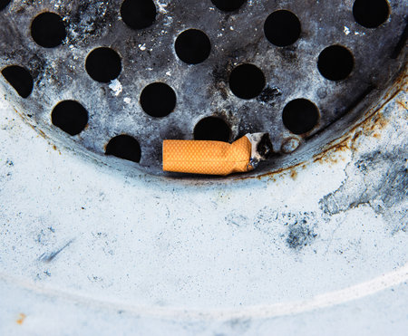 Closeup of a discarded cigarette butt stuck in a rusted metal grate of garbage bin. Nonsmoking, smoking harm, urban pollution, healthy and unhealthy lifestyle, littering, environmental concept.の写真素材