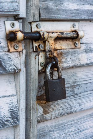 Rusty padlock and latch on white aged weathered closed wooden door. Closeup of rusted metal lock and old vintage rustic texture. Shabby chic design. Security safety and industrial concept. Copyspaceの写真素材