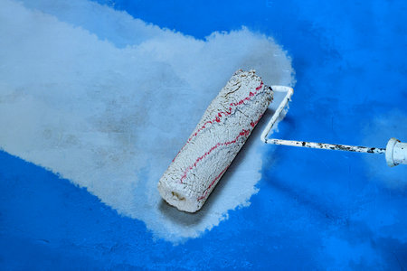Creative graphic concept of paint roller applying fresh white color paint onto the blue concrete wall. Process of home renovation, improvement and makeover. Copyspace.の写真素材