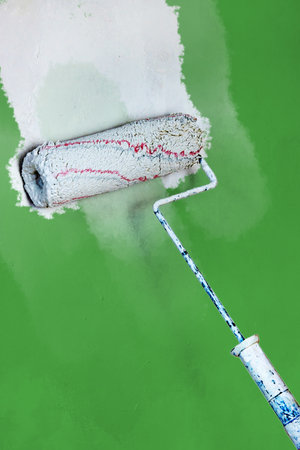 Creative graphic concept of paint roller applying fresh white color paint onto the green concrete wall. Process of home renovation, improvement and makeover. Copyspace.の写真素材