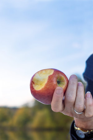 Closeup of a hand holding a red apple with a bite taken out of it. Perfect for themes of health, nutrition, and fresh produce. Hand presenting a bitten red apple, in an outdoor setting. Copy spaceの写真素材