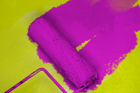 Creative graphic concept of paint roller applying fresh purple lilac paint onto the yellow color concrete wall. Process of home renovation, improvement and makeover. Copy space.の写真素材
