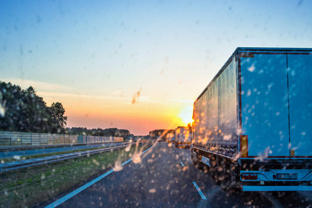 Highway traffic during sunset with trucks and cars through a dirty windshield, showcasing transportation, logistics, road safety and the challenges of visibility while driving on long journeys.の写真素材