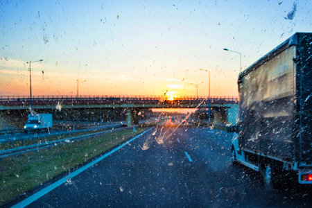 Highway traffic during sunset with trucks and cars through a dirty windshield, showcasing transportation, logistics, road safety and the challenges of visibility while driving on long journeys.の写真素材