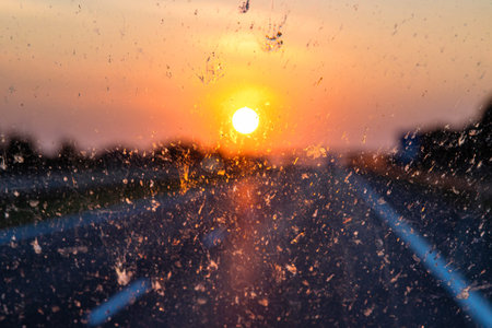 Blurry highway through a smudged dirty car windshield,  affecting visibility during sunset, emphasizing highway traffic safety concerns and the importance of clean glass for safe travel.の写真素材