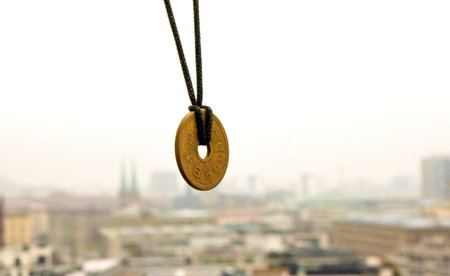 Lucky japanese 5 yen coin necklace displayed with a blurred foggy Berlin skyline in the background, symbolizing good fortune and cultural heritage. Selective focus. Copy spaceの写真素材