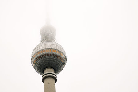 Berlin TV tower in dense fog, iconic Alexanderplatz landmark disappearing into mist. Foggy Fernsehturm in Berlin, Germany. Cloudy sky on background. Copy spaceの写真素材