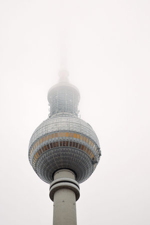 Berlin TV tower in dense fog, iconic Alexanderplatz landmark disappearing into mist. Foggy Fernsehturm in Berlin, Germany. Cloudy sky on background. Copy spaceの写真素材