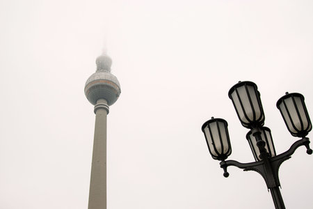 Minimalist Berlin skyline view with Berlin TV tower disappearing into fog. Foggy Fernsehturm in Berlin, Germany. Vintage street lamps in the foreground. Cloudy sky on background. Copy spaceの写真素材