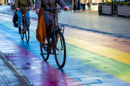 Two cyclists ride stylish black bicycles across a vibrant rainbow crosswalk on a Regenboogvlag in...