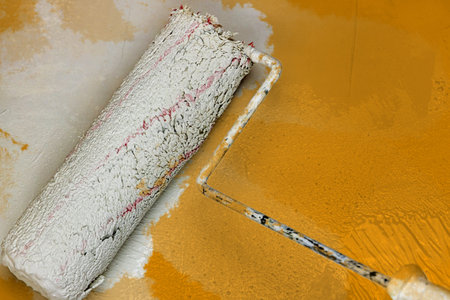 Creative graphic concept of paint roller applying fresh orange color paint onto the white concrete...
