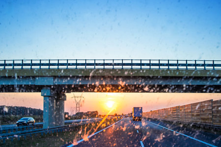 Highway and bridge at sunset through a dirty windshield, emphasizing road safety and the challenges...