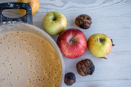 Top view of the vintage pot with homemade apple pie batter on a rustic white wooden table, surrounded by fresh apples and walnuts.の写真素材