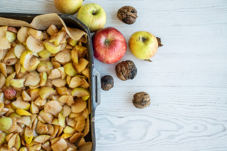 Top view of a black baking tray filled with chopped apples and whole walnuts on the white rustic wooden table.の写真素材