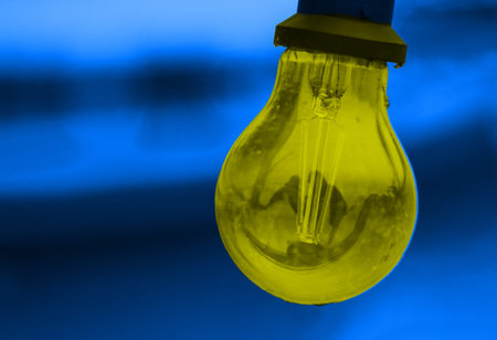 Striking contrast of vibrant artistic yellow glass bulb hanging in front of a rich blue background. Innovation, energy, and futuristic lighting design concept. Copy spaceの写真素材
