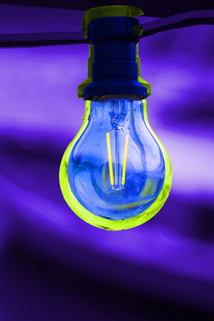 Dark blue glass bulb with socket on an lilac purpur background. Abstract concept image of colorful...