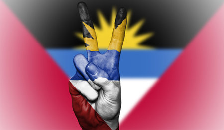 Hand showing the international symbol for peace, decorated in the national colors of Antigua and Barbudaの写真素材