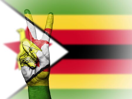 Hand showing the international symbol for peace, decorated in the national colors of Zimbabweの写真素材