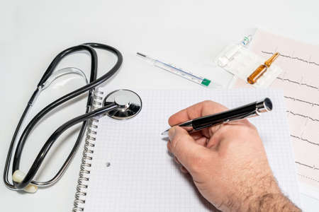 Hand of cardiologist doctor writing the diagnosis on block notes after seeing the electrocardiogramの写真素材
