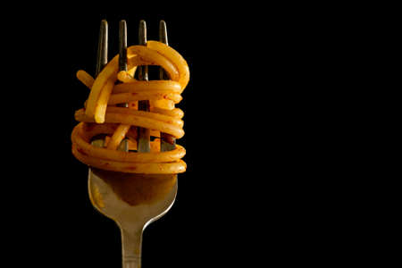 Close up of Italian Spaghetti on a fork with tomato sauce on black background. Typical Italian Food, stereotype to identify Italian culture. High quality photoの写真素材