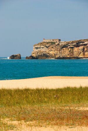 Cliff with lighthouse, sandy beach and green grass, Nazare, Portugalの写真素材
