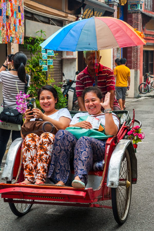 GEORGE TOWN, MALAYSIA - OCTOBER 24: Man driving rickshaw with two smiling women in George town...